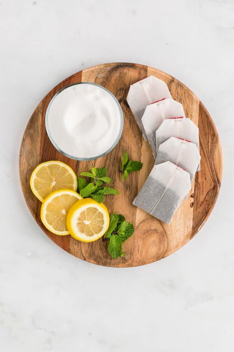 Tea bags, lemon slices and sugar in a bowl on a wooden cutting board
