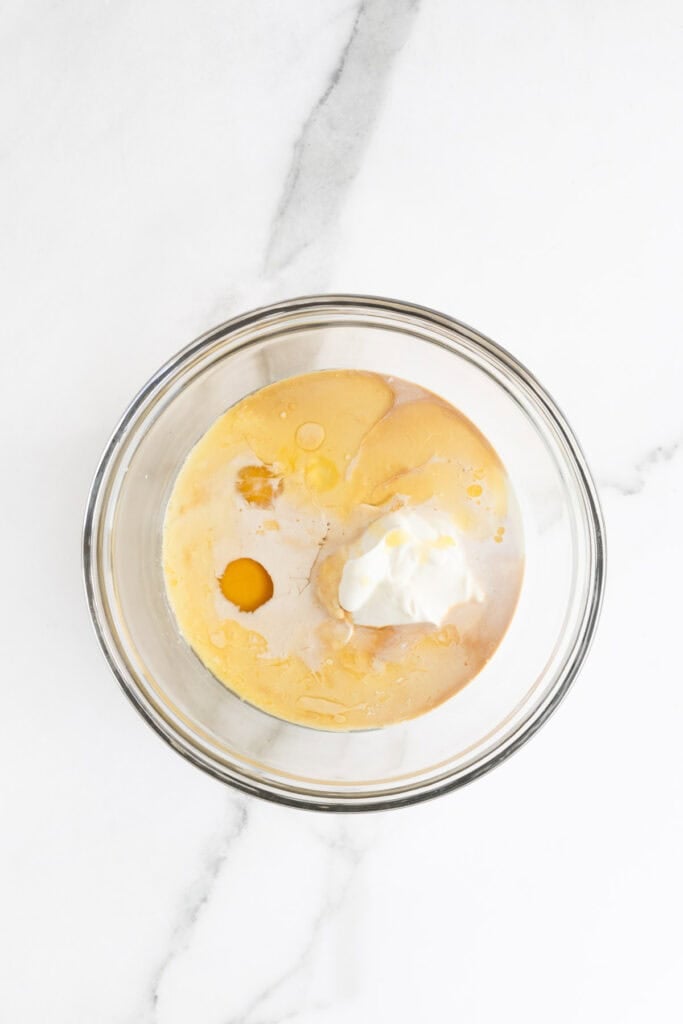 Eggs, half and half, sour cream, melted butter and vanilla in a glass bowl on white countertop