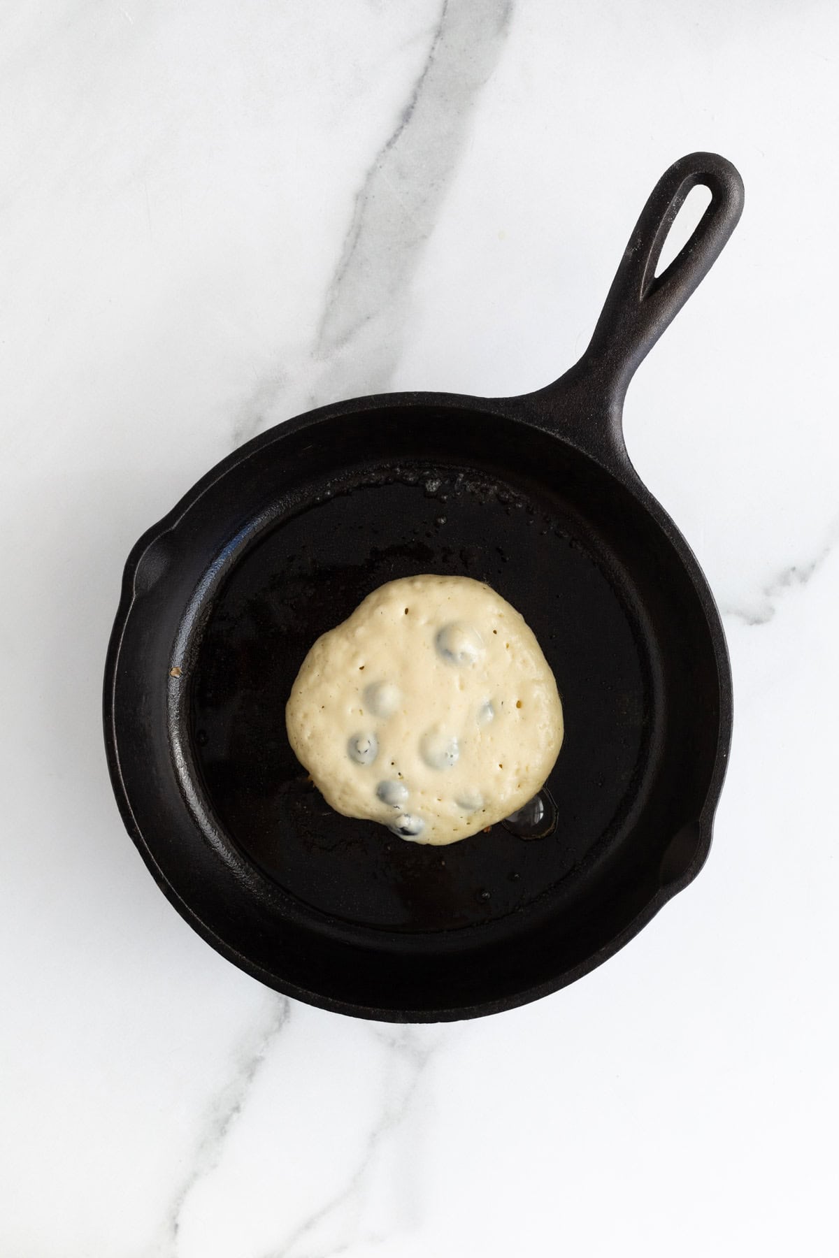 Pancake cooking in a cast iron skillet with edges browning