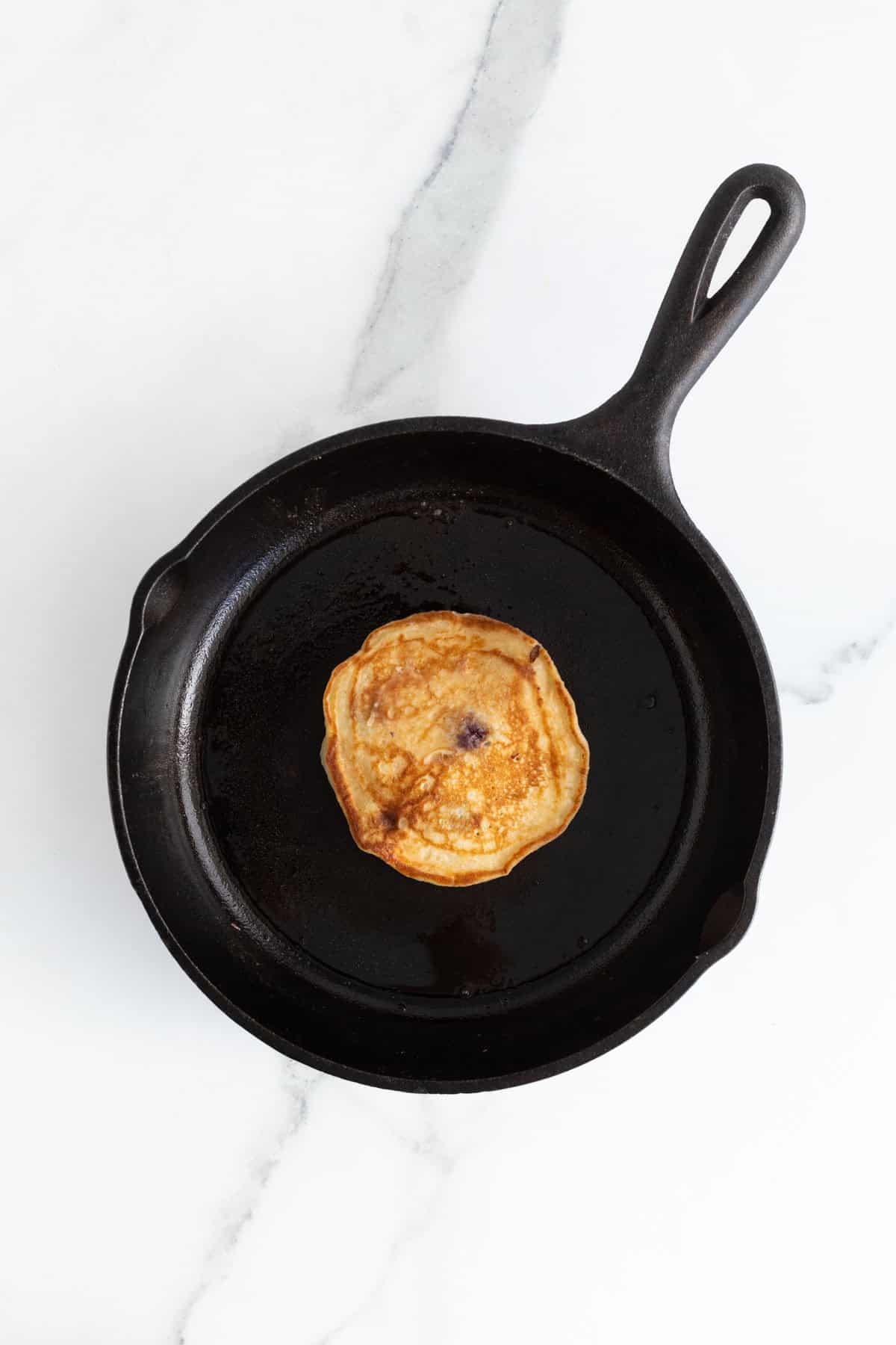 A flipped blueberry pancake in a cast iron skillet