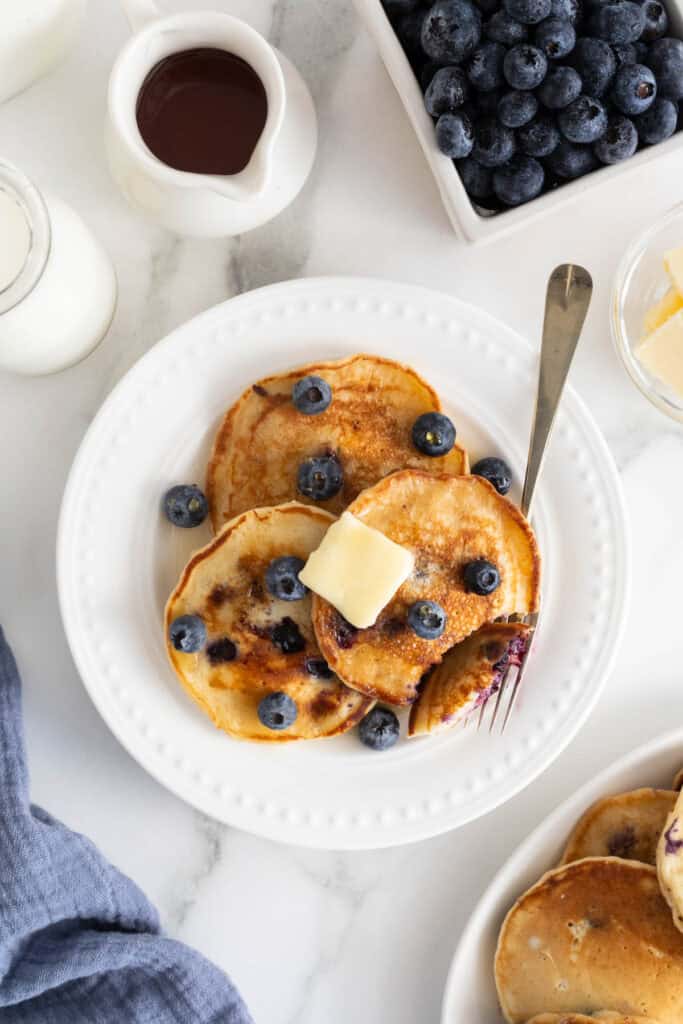 Three blueberry pancakes on a white plate with syrup and butter ready to serve