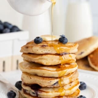 A stack of homemade blueberry pancakes with syrup pouring over them