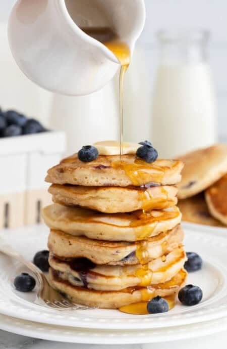 A stack of homemade blueberry pancakes with syrup pouring over them