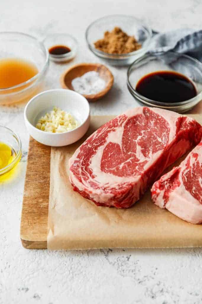 All the ingredients to make this grilled ribeye steak recipe including raw steak, salt, garlic and brown sugar