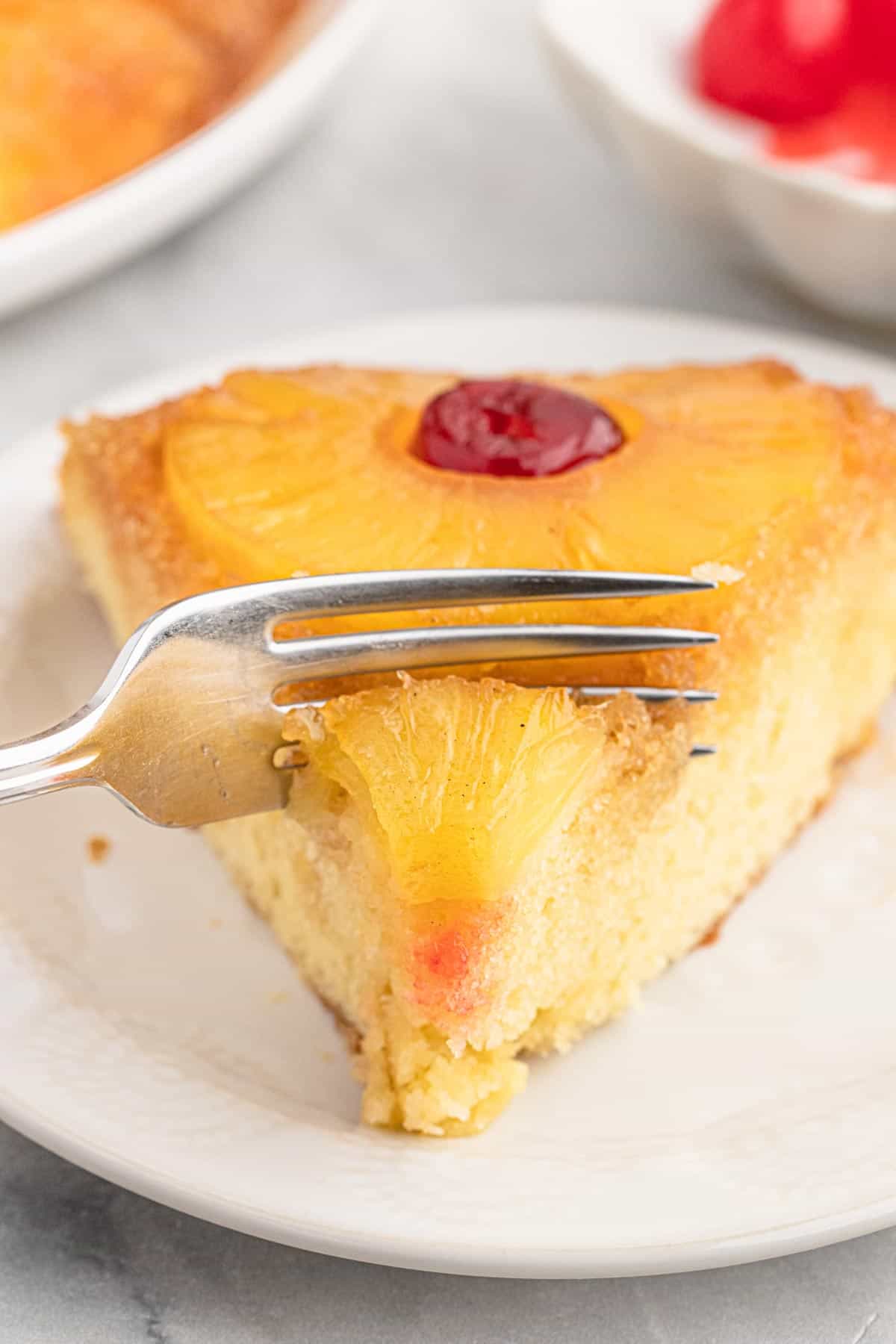 Slice of pineapple cake on a plate with a fork cutting a bite.