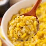 A large wooden spoon digging into sauteed yellow squash in a white bowl