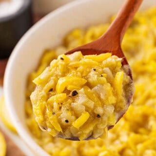 A large wooden spoon digging into sauteed yellow squash in a white bowl