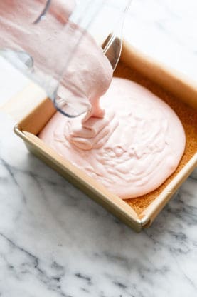 No bake strawberry cheesecake mixture being poured over a graham cracker crust in a baking pan