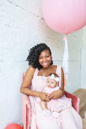 A seated Jocelyn holding her daughter with a pink balloon in the background