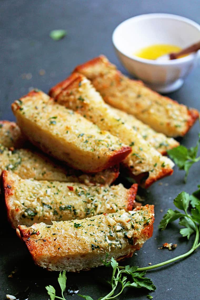 A delicious loaf of homemade garlic bread in slices against a black background