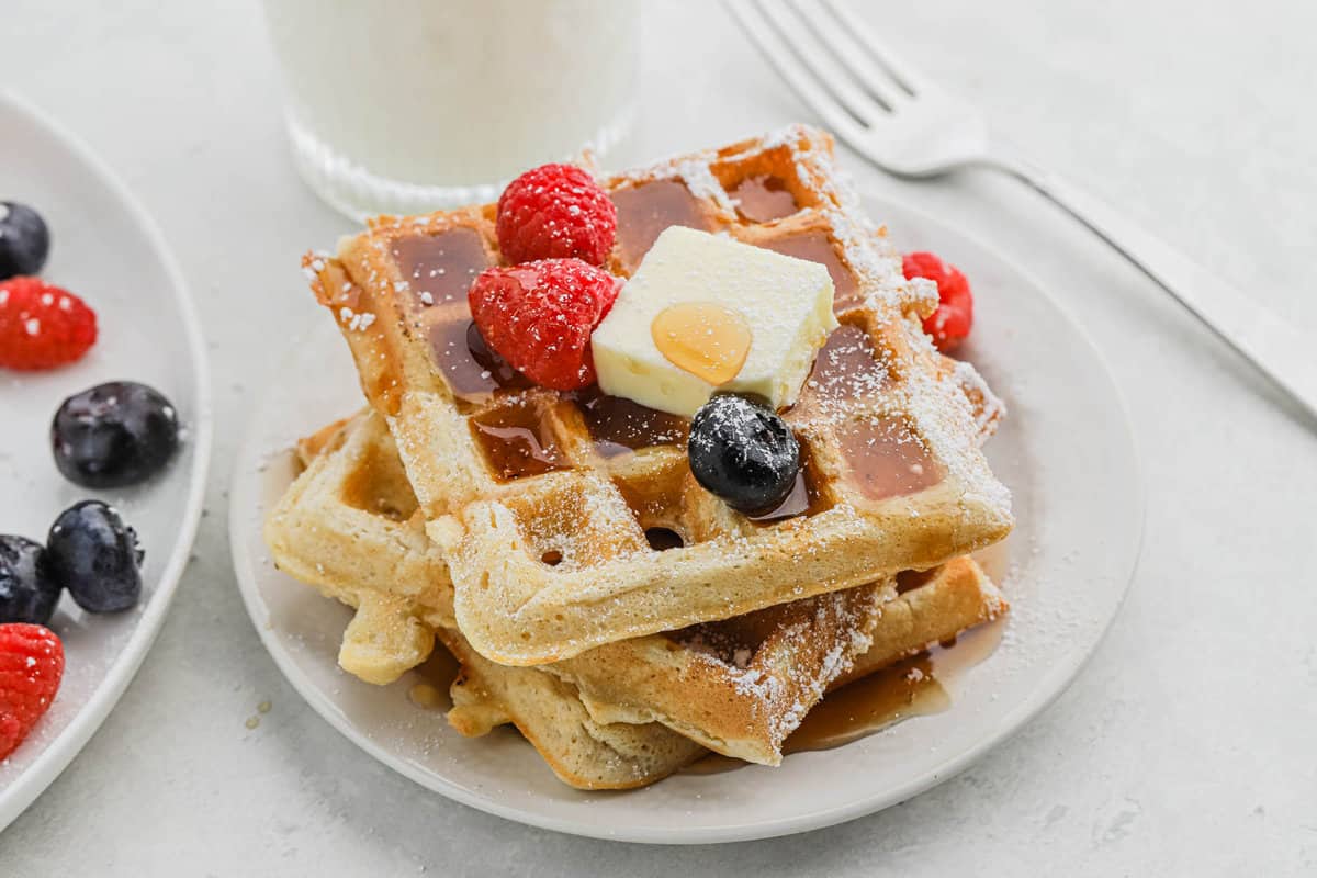 A plate of buttermilk waffles on a plate topped with syrup, butter, and fresh fruit.