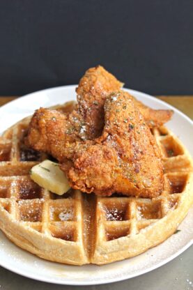 A top down shot of chicken and waffles with butter and syrup melting down with a black background