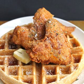 A top down shot of chicken and waffles with butter and syrup melting down with a black background