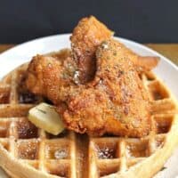 A top down shot of chicken and waffles with butter and syrup melting down with a black background