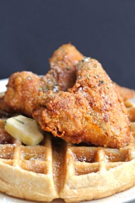 Two fried chicken wings laying on top of a buttermilk waffle with a butter pat ready to serve