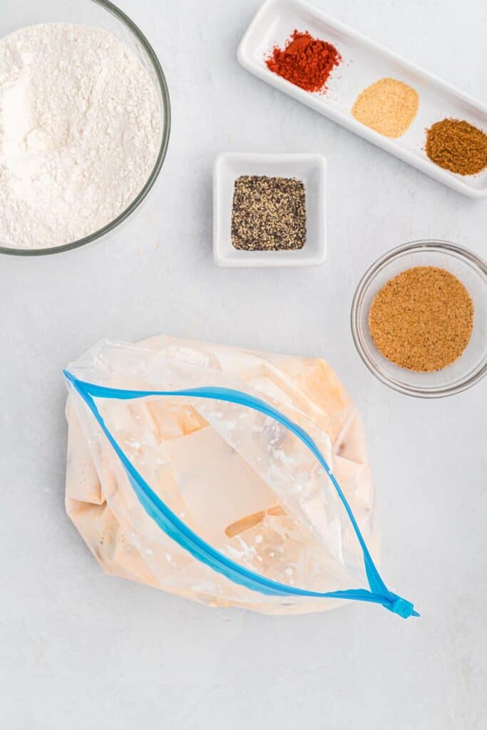 Chicken gizzards in a bag with buttermilk marinating on a white countertop with seasonings nearby