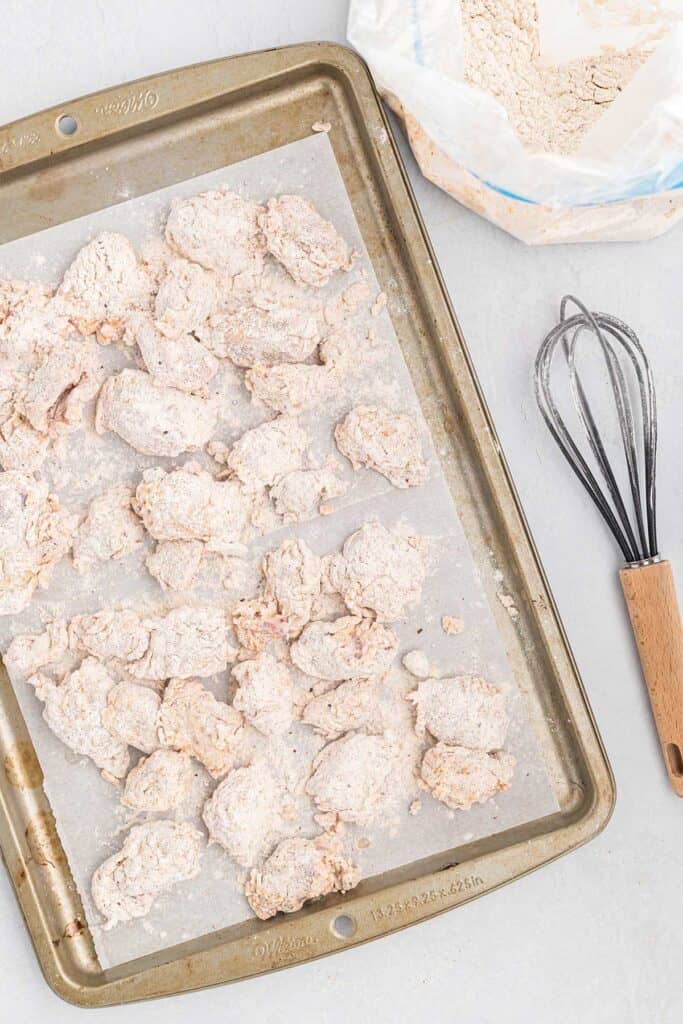 Chicken gizzards coated in flour on a baking tray on a white countertop.