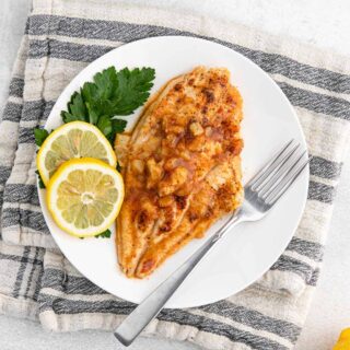 Grilled catfish recipe with pineapple marinade on a plate with a fork and garnished with lemon slices.