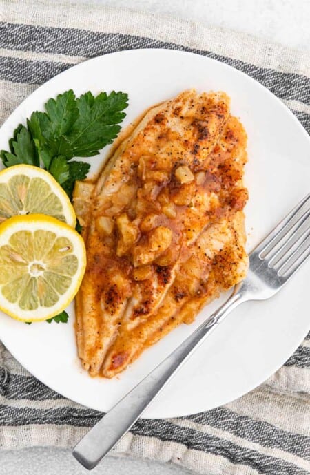 Grilled catfish recipe with pineapple marinade on a plate with a fork and garnished with lemon slices.