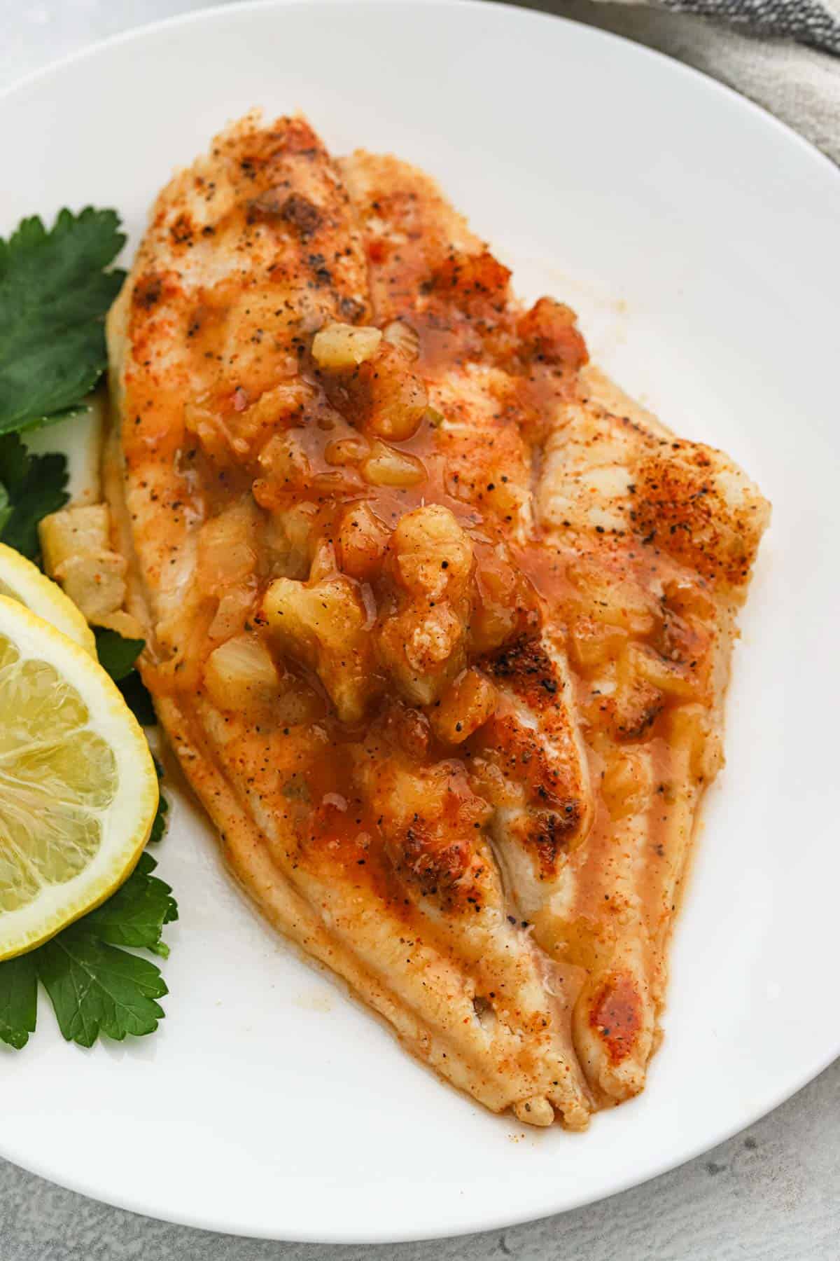 A piece of fish on a plate with parsley and lemon slices.