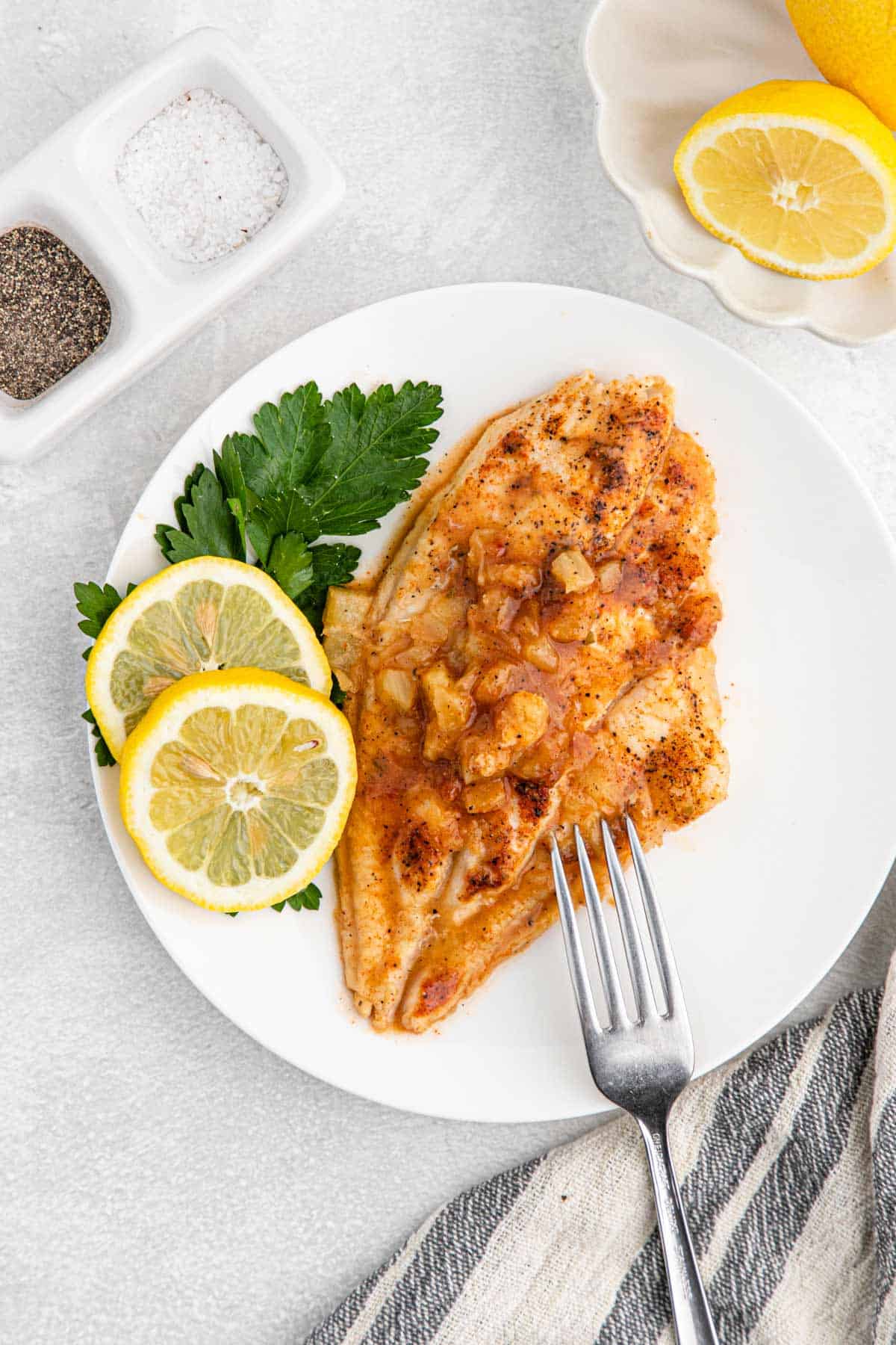 Pineapple Honey Bourbon Grilled Catfish on a white plate with parsley and lemon slices.