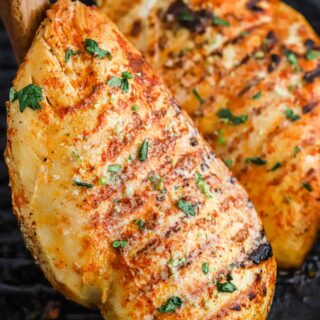 Two tequila lime chicken breasts in a skillet with one being lifted out