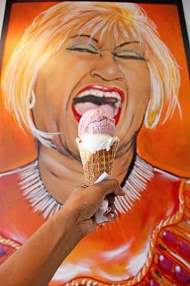 Jocelyn holding a waffle cone with two scoops of ice cream in front of a painting of singer Celia Cruz at Azucar Ice Cream Company