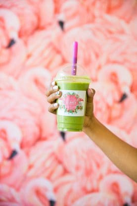 Jocelyn holding a green smoothie in front of a painting of a flock of pink flamingos at Dreamer South Beach