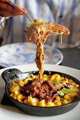 Mouthwatering carne asada mac and cheese served at Finka Table and Tap in a mini black cast iron skillet and dangled from a fork