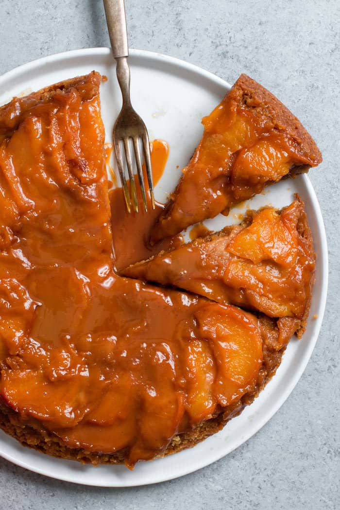 Overhead shot of a dump cake featuring caramel and peaches on a white plate with several slices missing. 