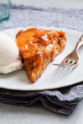 One slice of this caramel peach dump cake with a scoop of vanilla ice cream on a white plate with a fork