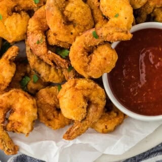 The best fried shrimp on a white plate lined with parchment with lemon wedges and cocktail sauce