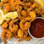 deep fried shrimp on a parchment paper with lemon wedges and cocktail sauce ready to serve