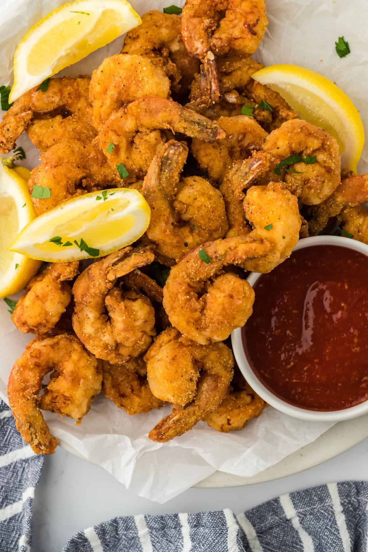 deep fried shrimp on a parchment paper with lemon wedges and cocktail sauce ready to serve