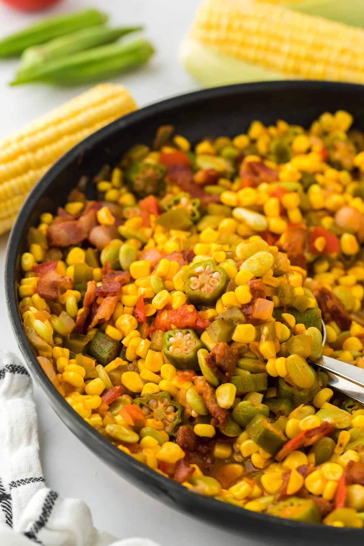 A Southern succotash recipe in a pan with corn and green peppers in the white background