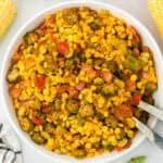 Southern succotash in a white bowl with a tomato and corn in the background ready to serve