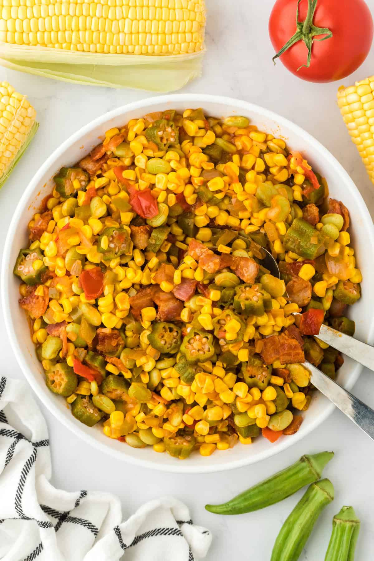 Southern succotash in a white bowl with a tomato and corn in the background ready to serve