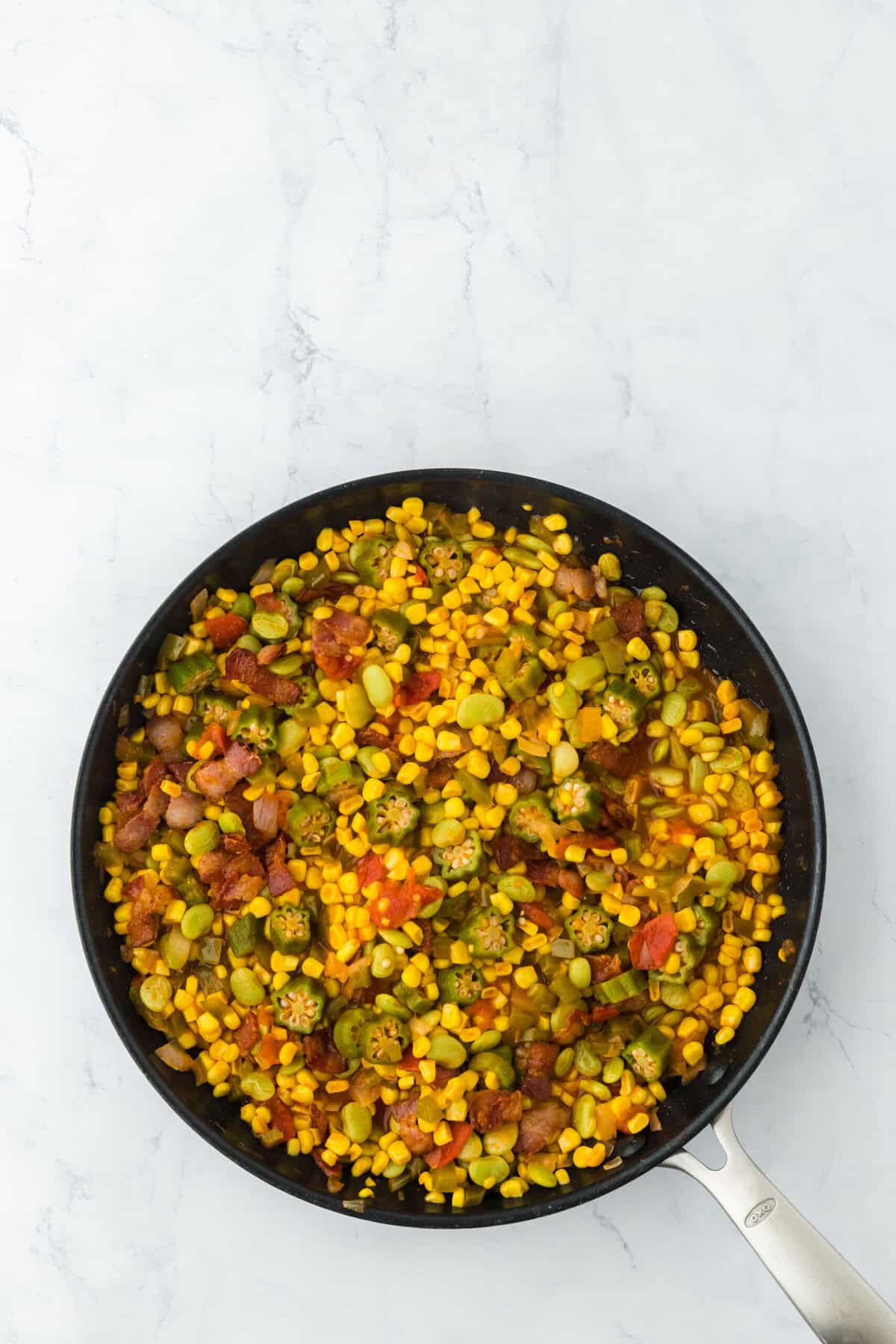 Southern succotash with bacon on top in pan on white background