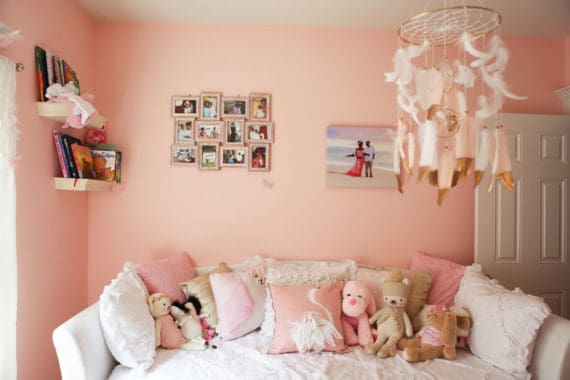 Baby Cakes Nursery featuring a white day bed with pillows and stuffed animals and framed photos and books on book shelves on the pink walls