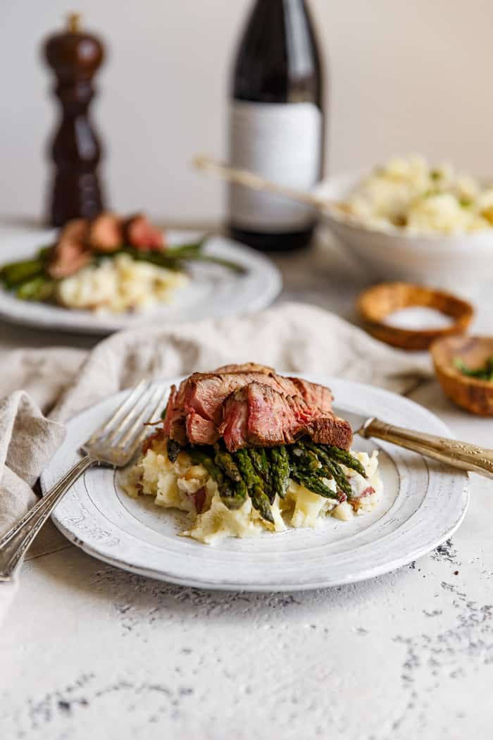 Chipotle Steak Au Poivre plated for two for Valentine's Day with asparagus and mashed potatoes and a bottle of wine in the background