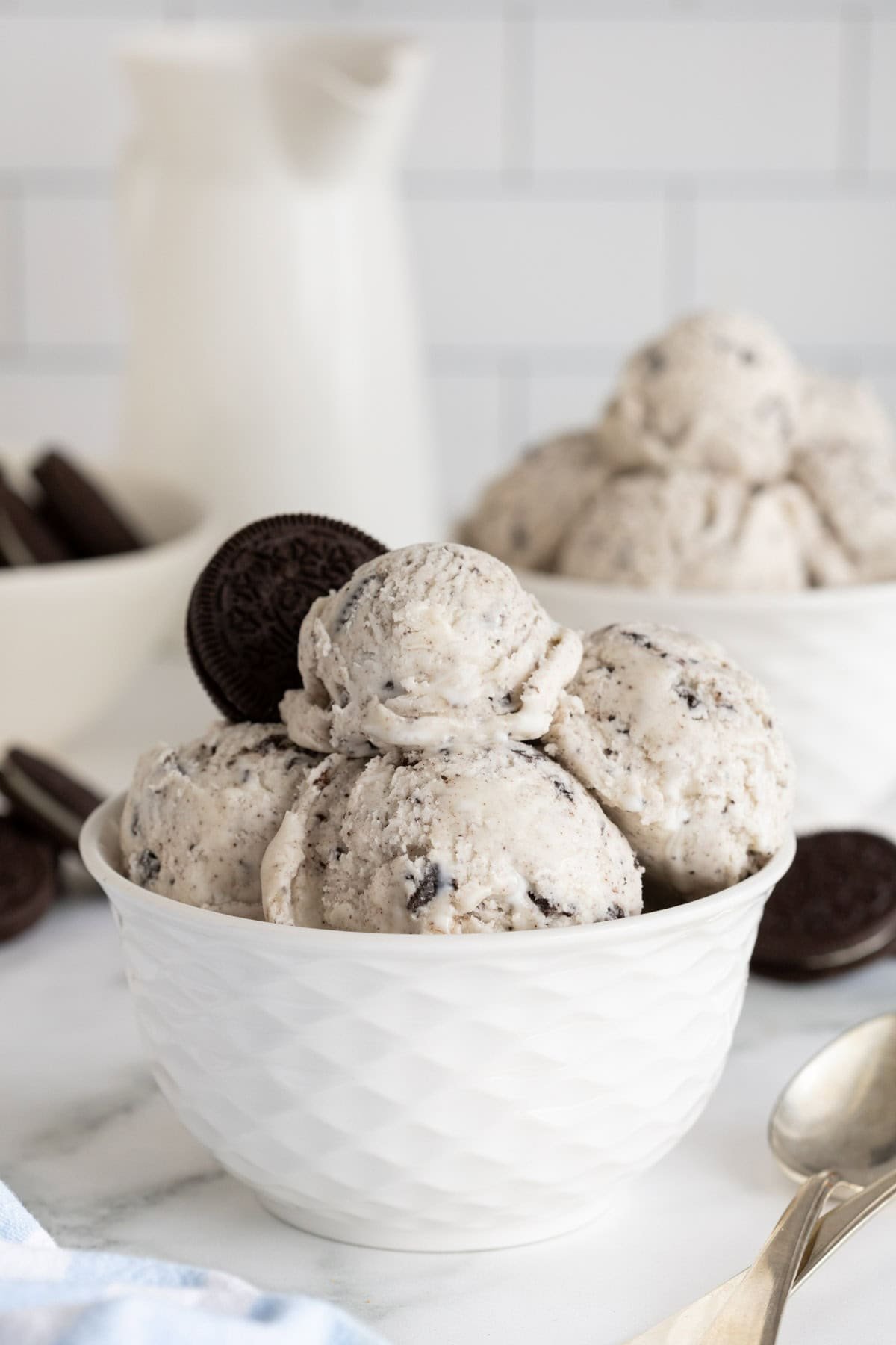Cookies and cream ice cream in a textured white bowl, topped with a whole Oreo, with more ice cream in the background