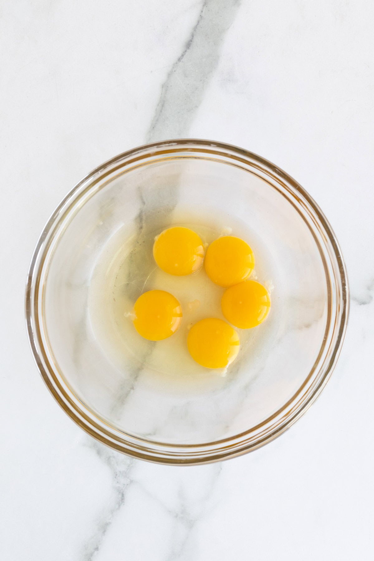 Raw egg yolks in a clear glass mixing bowl