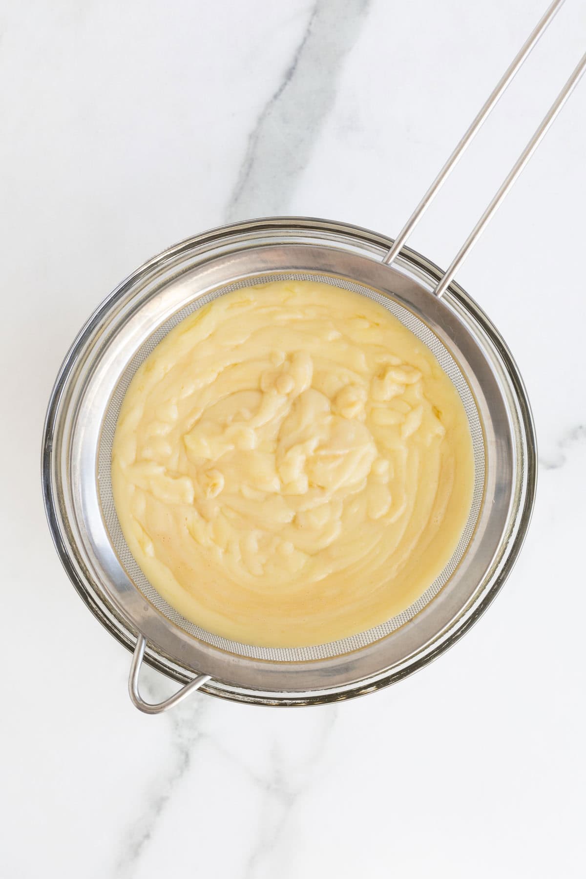 Custard being strained through a fine mesh sieve into a bowl