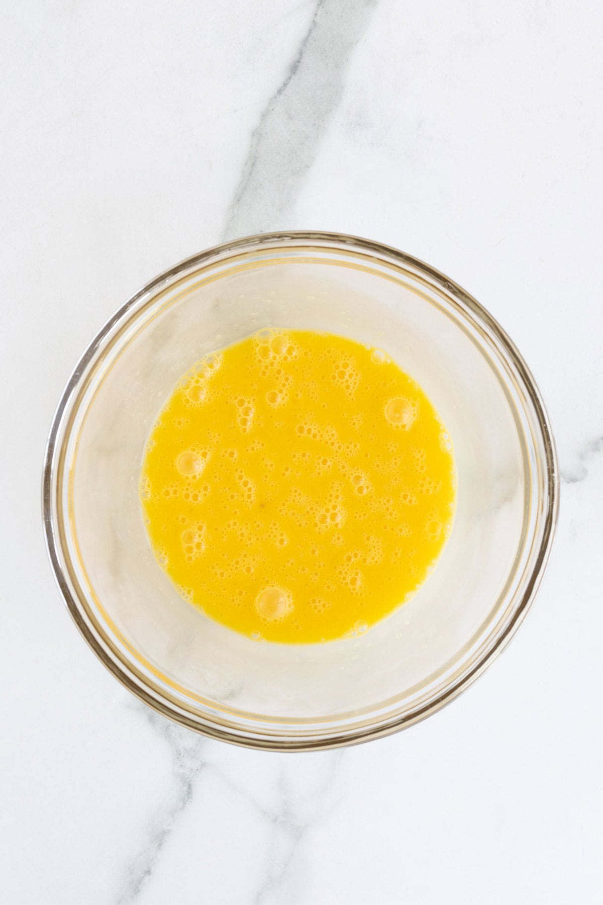  Beaten egg yolks in a glass bowl, forming a smooth yellow mixture