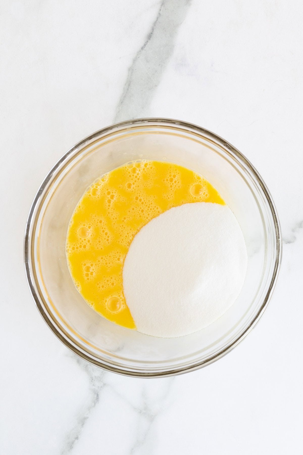 Egg yolks mixed with a heap of granulated sugar in a glass bowl