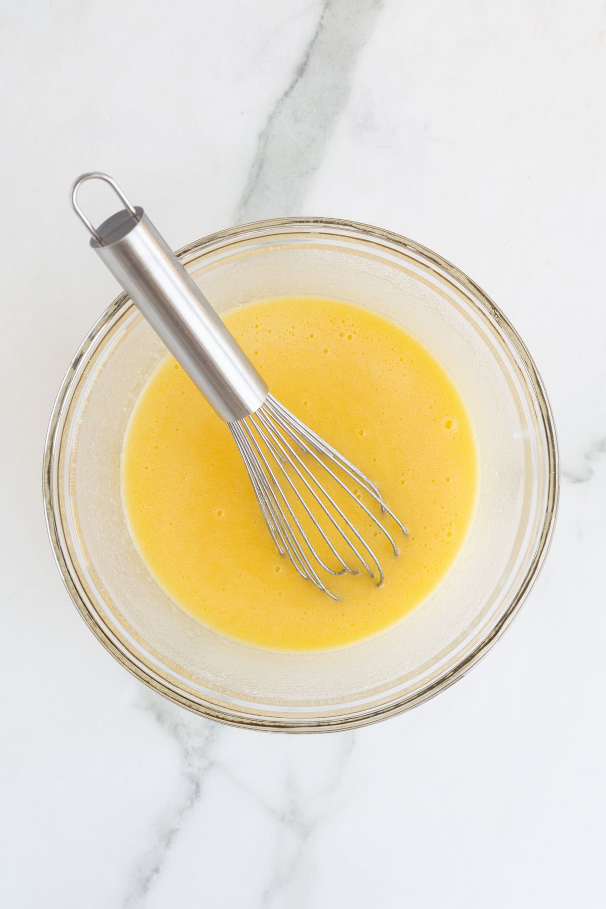 Tempered custard mixture with whisk resting in the bowl