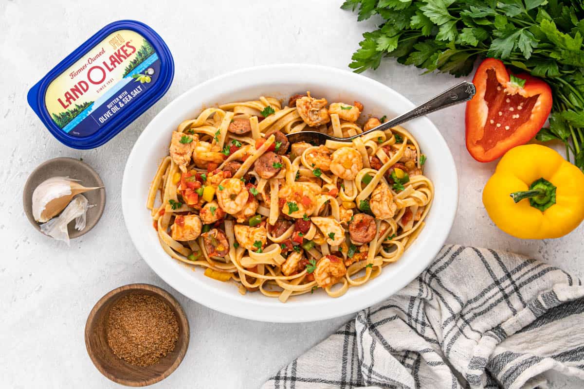 Overhead shot of a large platter of jambalaya pasta surrounded by a bowl of cajun spice blend, peppers, garlic, and butter.