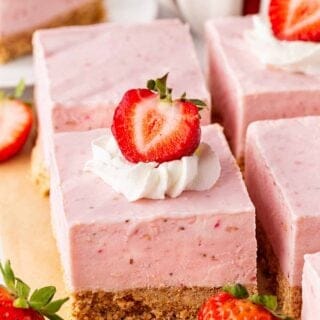 Strawberry cheesecake bars topped with whipped cream and fresh strawberries, surrounded by whole and sliced strawberries