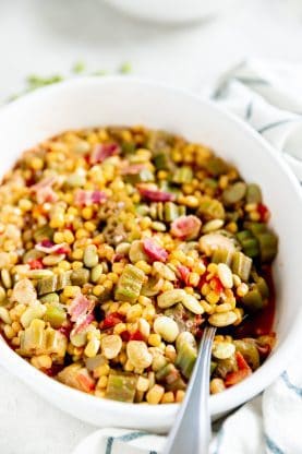 A spoon inside of Corn Succotash recipe ready to serve out of large white bowl