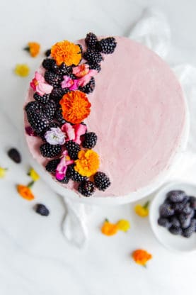 Overhead shot of a completed three layer chocolate cake with blackberry buttercream and topped with fresh blackberries and flowers